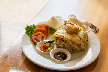 A plate of fried rice with an omelet and shrimp, served with soy sauce and vegetables as garnish, on a wooden table