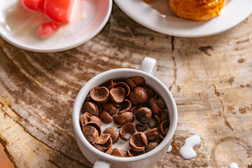 A child is pouring a glass of fresh milk into their chocolate flavored cereal, representing a kids' breakfast concept