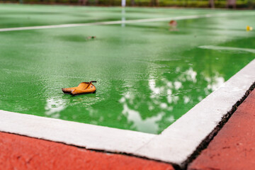 A wet tennis court after the rain, with puddles reflecting the sky and a damp playing surface