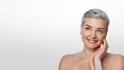 Skincare And Beauty. Gorgeous Nude Middle Aged Woman Touching Her Soft Skin And Looking Away At Copy Space On Light Background, Panorama