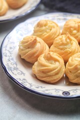 Kue Sus Isi Vla or soes cake (Choux Pastry Cream Puff) is Crispy and airy choux pastry shell are filled with smooth and soft custard cream. served in a plate.
