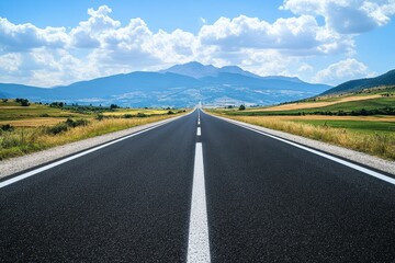 Asphalt road cuts through scenic landscape, mountains in background. Ideal for travel, journey, freedom concepts.