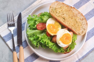 Sourdough bread open faced sandwiches with lettuce, tomatoes, egg and sausage. A healthy and delicious breakfast.
