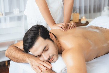 Caucasian man customer enjoying relaxing anti-stress spa massage and pampering with beauty skin recreation leisure in day light ambient salon spa at luxury resort or hotel. Quiescent