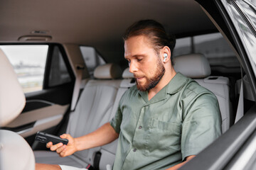 Young man using smartphone in the backseat of a car