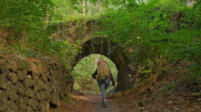 Backpacking hiker walking under abandoned bridge tunnel in a remote forest in slow motion, Rhine Valley, Germany