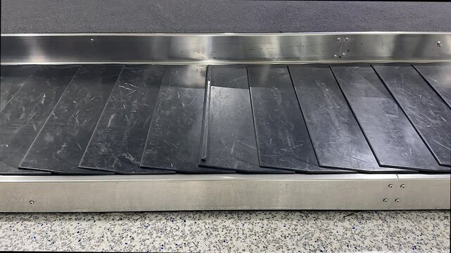 An empty luggage carousel is operating in a brightly lit airport arrivals hall