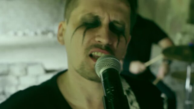 Fierce punk rock band performs with raw energy inside abandoned building. The singer belts into the mic, while the drummer pounds heavy beats. Clad in bold attire, they bring life to the empty space