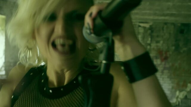 Bold female rocker leads the band, singing into mic with passion. Behind her, guitarist shreds fierce riffs as the drummer pounds rhythmic beats. Clad in edgy attire, they perform in empty building