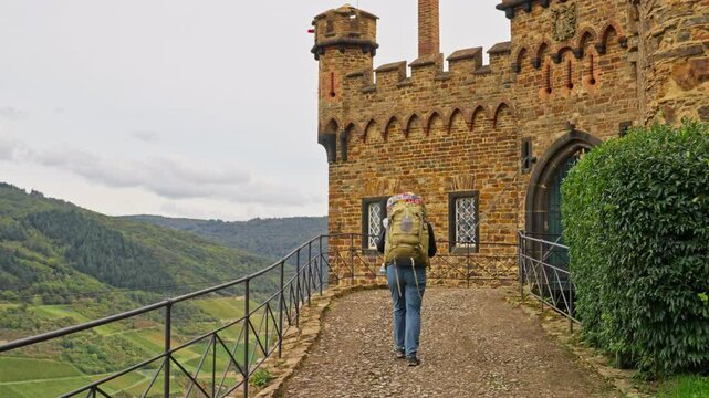 Hiker with large backpack walking on path leading to the entrance of a castle door, Rhine Valley, Germany
