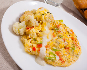 Delicious vegetable omelette served on white plate with cauliflowers, grated cheese and cream sauce..