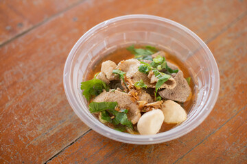 Clear pork noodle soup in a plastic cup on a wooden table with copy space