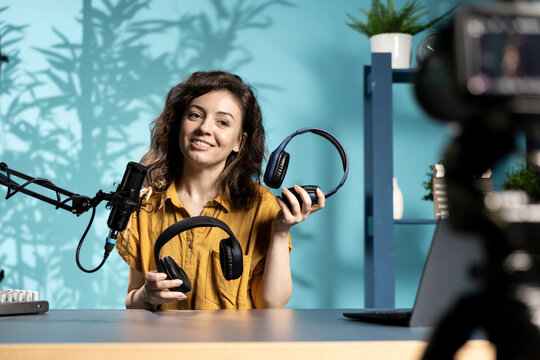 Jolly content creator in home studio filming headphones review for online streaming platforms. Upbeat media star hosts internet show, comparing music listening devices from different price ranges