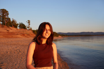 Portrait of a laughing girl. A happy girl walks on a sandy beach at sunset. Summer travel, vacations at sea.