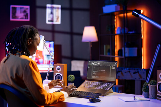 Software developer writes code on laptop screen while in apartment office using Java programming languages. Programmer remotely working on fixing database errors while working from home