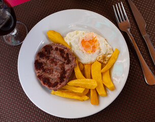 Appetizing roasted beef hamburger patty served with potatoes and egg on platter