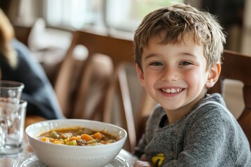 A young boy smiles as he eats a bowl of homemade vegetable soup
