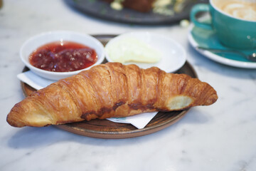 Delicious croissant served with jam and butter on a wooden plate