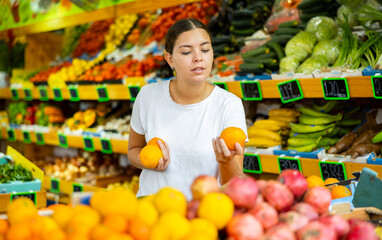 Happy smiling girl making purchases in supermarket, choosing fresh ripe oranges