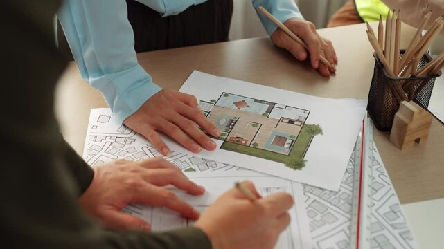 Professional engineer team discussion about house design on meeting table with architectural equipment and building blueprint scatter around at modern office. Focus on hand. Closeup. Delineation.