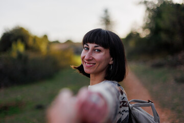 follow me. Beautiful female traveler with a backpack standing on the slope of a mountain ridge and...