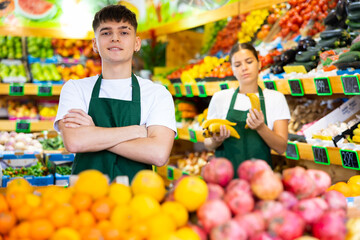 Handsome european male seller posing and offering different fresh fruit in supermarket