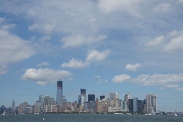 Fototapeta premium New York, Manhattan boasts a towering skyline with the Statue of Liberty standing proudly in the foreground. The calm water reflects the tall skyscrapers against a clear blue sky, creating an iconic