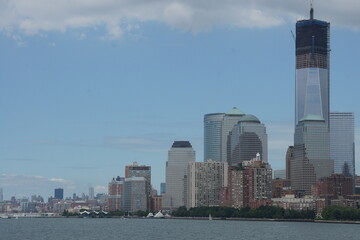 Obraz premium A vibrant New York, Manhattan skyline bathed in the warm glow of a sunset, with skyscrapers casting their reflections onto the still waters of the Hudson River. Bustling city life continues along