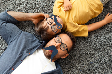 Festive mood. Young happy father and his little son wearing eyeglasses and holding photo props...