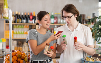 Couple young man and young woman scanning qr code for spices and seasonings at grocery store