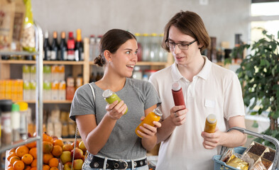 Youth girl and guy spouses hold bottles and choose consider smoothie in store. Market visitors pick...