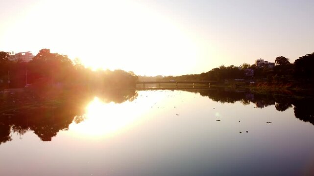 Sunset view of Godavari riverbank near Panchavati Hindu temple and Ganga Ghat in Nashik, Road bridge in background, Maharashtra, Drone shot