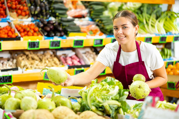 Portrait of young happy woman in apron selling organic zucchini in shop