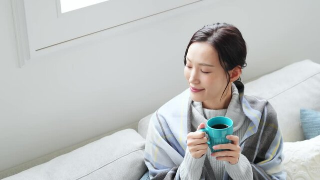 女性、飲む、寒い、冬、暖かい、コーヒー、笑顔、日本人、暖冬、対策、防寒、ストール、ショール、ブランケット、コピースペース、インテリア、リビングルーム、ライフスタイル、おしゃれ、リラックス、ほっこり、安心、ソファー、若い、寒暖差、紅茶、カップ、暖房、エアコン、マフラー、ポジティブ、快適、節電、室内、明るい、省エネ、爽やか、毛布、シンプル、キレイめ、きれいめ、寒さ、寒気、冷気、住宅、俯瞰、ハイアングル