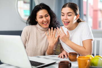Happy asian and caucasian women showing wedding rings during video call.