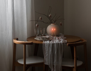 Festive Easter setting - easter bouquet in a ceramic vase, dishes, burning candles on a round wooden table in the living room