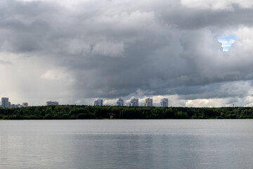 Obraz premium Residential buildings of the city on the horizon above the water of the lake Shartash in the Shartash Forest Park. Ekaterinburg