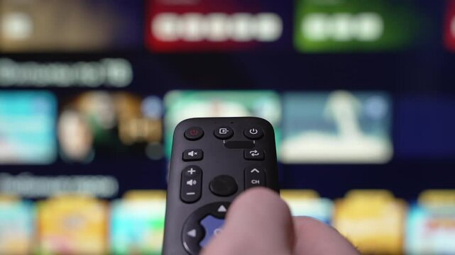 Person Browsing Streaming Services Using Remote Control. Hand Holding a Remote Control Browses Various Streaming Services On a Large Screen. Focused on the Hand. Turn Off smart TV. Internet TV