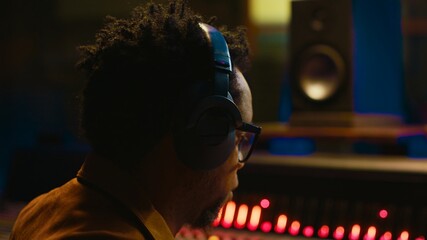 African american sound engineer using headphones to listen to audio recordings in post production,...