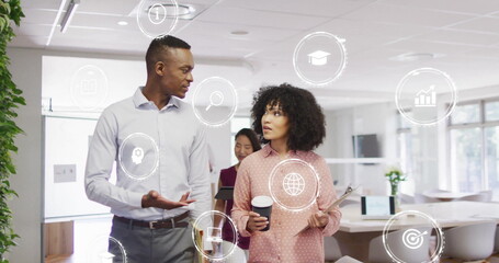 Image of media icons over diverse colleagues discussing work in office