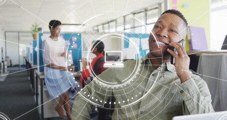 Image of media icons over diverse colleagues discussing work and talking on smartphone in office