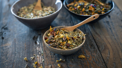 various organic herbal teas in ceramic bowls on a dark rustic wooden table - healthy living concept