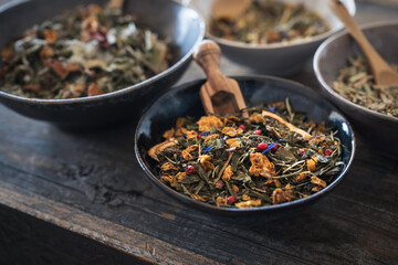 various organic herbal teas in ceramic bowls on a dark rustic wooden table - healthy living concept