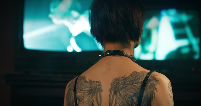 Sexy lady with tattooed wings on back looking at old TV displays with her image . Harassment and victimization, kidnapping and abduction, thriller movie and nightmare concept, rearview of woman