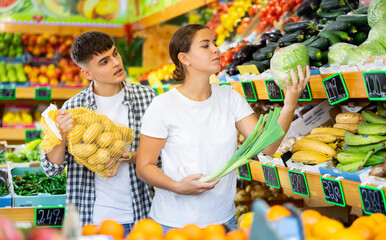 Positive couple choosing fresh foods in fruit and vegetable section of supermarket