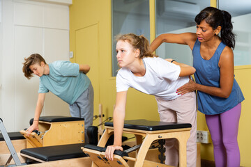 Pilates instructor helping gyrl doing exercises on reformer apparatus at sport gym