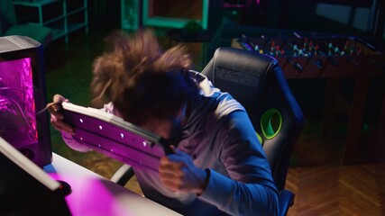 Angry gamer raging after losing against opponent in online esports competition. Upset player smashing keyboard on his head after being defeated by enemy in videogame internet tournament