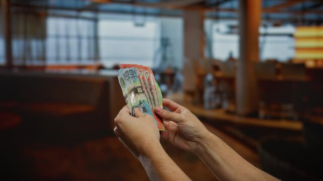 Man counting australian dollars indoors in a dimly lit caf&eacute;, showcasing business and currency exchange in a casual restaurant setting.