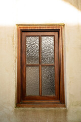 Wooden-framed window with textured glass set in a stucco wall
