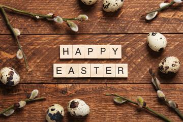 Text Happy Easter made of wooden blocks with sprigs of willow, quail eggs, feathers on a warm wooden background